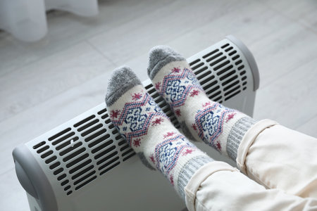 Woman warming feet on electric heater at home, closeupの写真素材