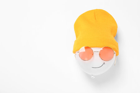 Funny face made of balloon, hat and sunglasses on white background, top view. Space for text
