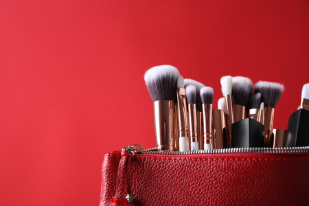 Bag with makeup brushes and cosmetic products on red background. Space for textの写真素材