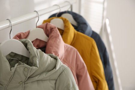 Different warm jackets hanging on rack indoors, closeupの写真素材