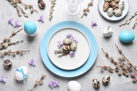 Festive Easter table setting with painted eggs and floral decor on light gray background, flat layの写真素材