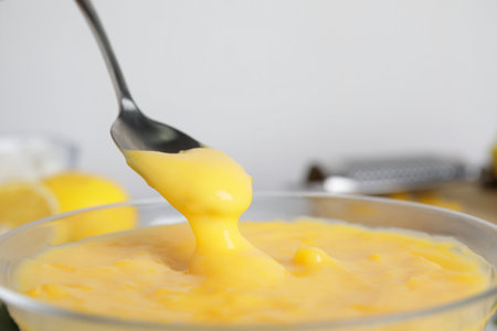 Spoon with delicious lemon curd above bowl, closeupの写真素材