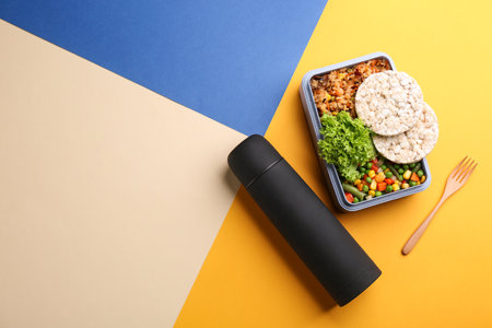 flask and lunch box with food on color background, flat lay. Space for text