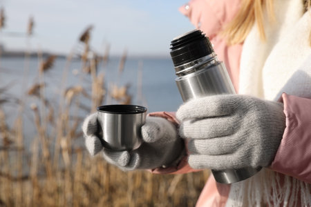 Woman pouring hot drink into cup from flask outdoors, closeupの写真素材