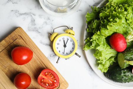 Alarm clock and vegetables on white marble table, flat lay. Meal timing conceptの写真素材
