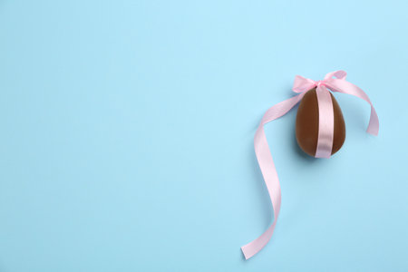 Sweet chocolate egg with pink bow on light blue background, top view. Space for textの写真素材