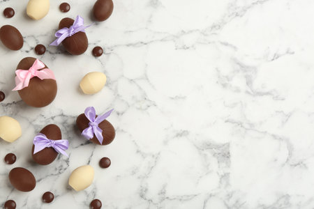 Sweet chocolate eggs and candies on white marble table, flat lay. Space for textの写真素材