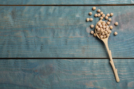 Raw chickpeas with spoon on blue wooden table, flat lay. Space for textの写真素材