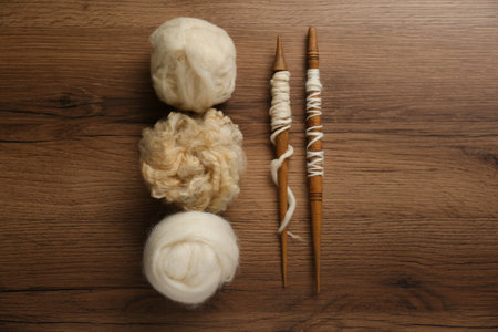 Soft white wool and spindles on wooden table, flat layの写真素材