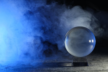 Magic crystal ball on gray table and smoke against dark background, space for text. Making predictionsの写真素材