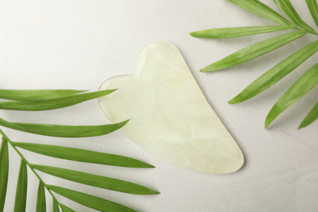 Jade gua sha tool and green leaves on gray table, flat layの写真素材