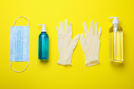 Medical gloves, mask and hand sanitizers on yellow background, flat layの写真素材