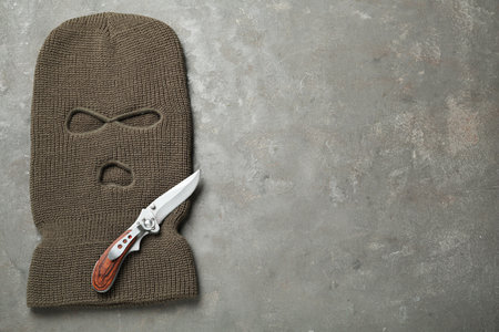 Beige knitted balaclava and knife on gray table, top view. Space for textの写真素材