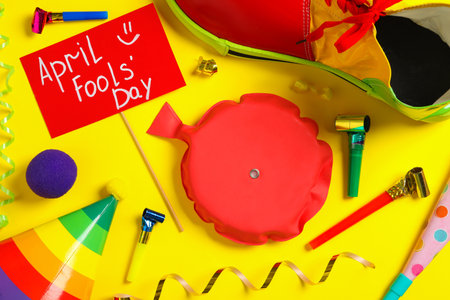 Sign with phrase April Fools' Day and different clown's accessories on yellow background, flat layの写真素材