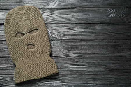 Beige knitted balaclava on black wooden table, top view. Space for textの写真素材