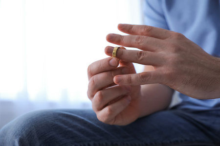 Man taking off wedding ring on blurred background, closeup. Divorce conceptの写真素材