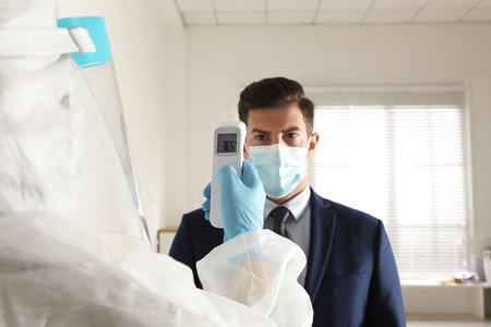 Doctor measuring man's temperature in office closeup. Prevent spreading of Covid-19の写真素材