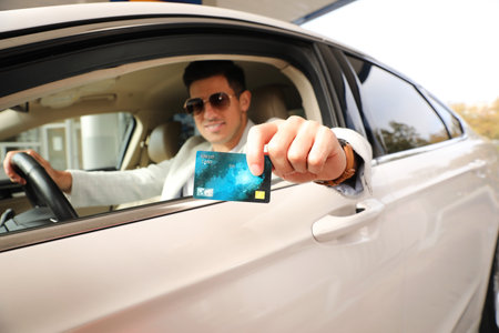 Man sitting in car and showing credit card at gas station, focus on handの写真素材