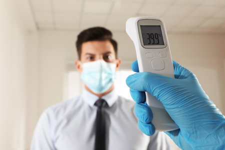 Doctor measuring man's temperature in office closeup. Prevent spreading of Covid-19の写真素材