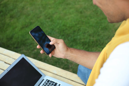 Man with smartphone and laptop in park, closeupの写真素材