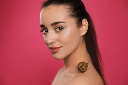 Beautiful young woman with snail on her neck against pink backgroundの写真素材