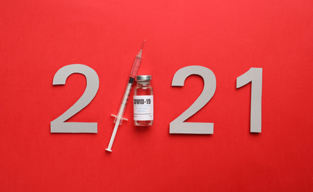 Paper numbers, syringe and vial with coronavirus vaccine forming 2021 on red background, flat layの写真素材