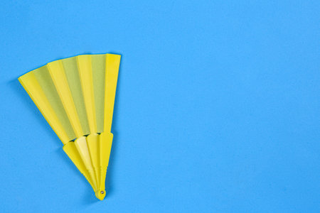 Yellow hand fan on light blue background, top view. Space for text