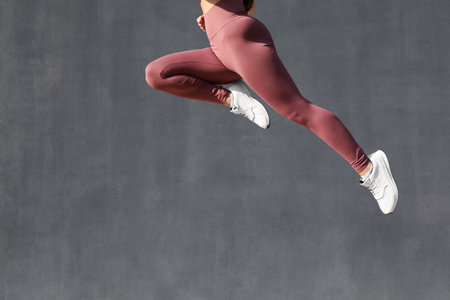 Young woman in stylish sports wear jumping on gray background, closeupの写真素材