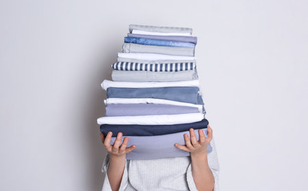 Woman holding stack of clean bed linens on white backgroundの写真素材