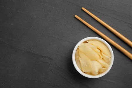 Pickled ginger in bowl and chopsticks on black table, flat lay. Space for textの写真素材