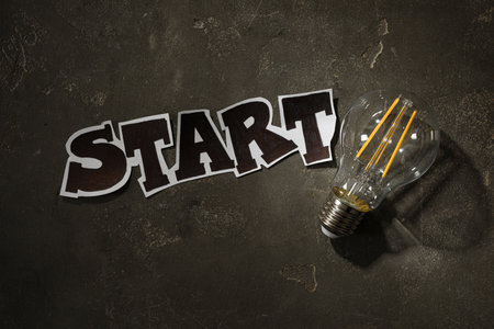 Vintage lightbulb and word Start on gray stone background, flat layの写真素材