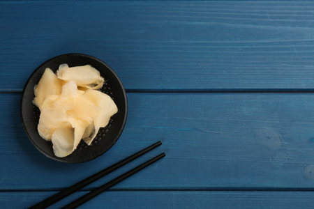 Spicy pickled ginger and chopsticks on blue wooden table, flat lay. Space for textの写真素材