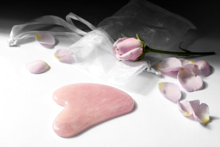 Rose quartz gua sha tool and flower on white tableの写真素材