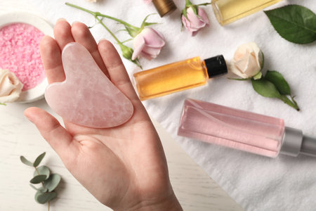Woman with rose quartz gua sha tool at white wooden table, top viewの写真素材
