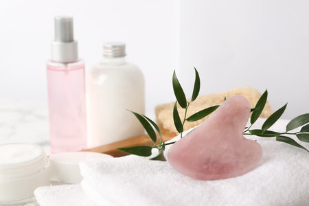 Rose quartz gua sha tool, cosmetic products and towel on tableの写真素材