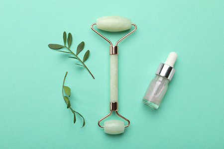 Natural face roller, cosmetic product and leaves on turquoise background, flat layの写真素材