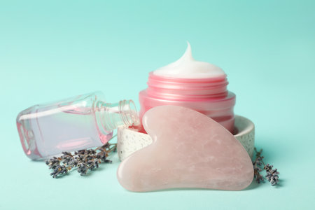 Rose quartz gua sha tool, cosmetic products and dried lavender flowers on light blue backgroundの写真素材