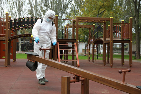 Woman wearing chemical protective suit with disinfectant sprayer on playground. Preventive measure during coronavirus pandemicの写真素材