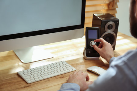 Man using remote to control audio speakers at table indoors, closeupの写真素材
