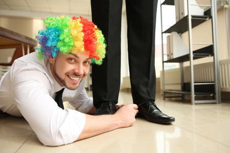 Man with clown wig tying shoe laces of his colleague together in office, closeup. funny jokeの写真素材