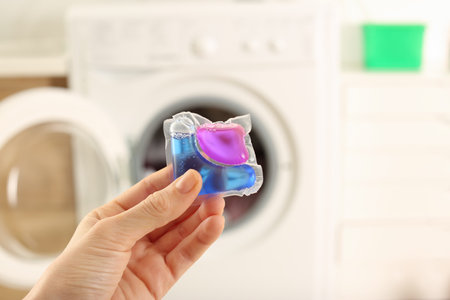 Woman holding laundry detergent capsule near washing machine indoors, closeupの写真素材