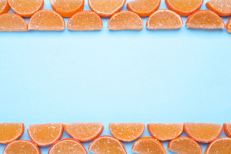 Delicious orange marmalade candies on light blue background, flat lay. Space for textの写真素材
