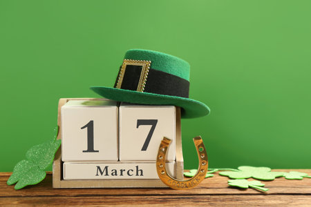 Composition with leprechaun hat and block calendar on wooden table against green background. St Patrick's Day celebrationの写真素材