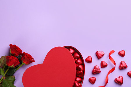 Heart shaped chocolate candies, ribbon and bouquet on violet background, flat lay. Space for textの写真素材
