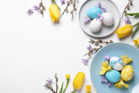 Festive Easter table setting with painted eggs and floral decor on white background, flat lay. Space for textの写真素材