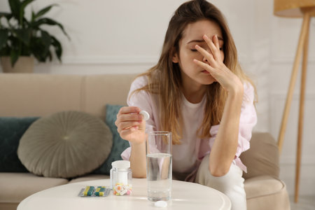 Woman putting medicine for hangover into glass of water at homeの写真素材