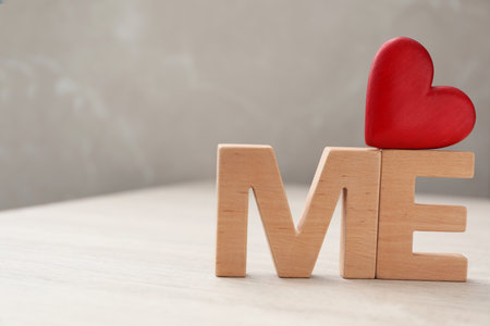 Phrase Love Me made of red heart and wooden letters on white table, closeup. Space for textの写真素材