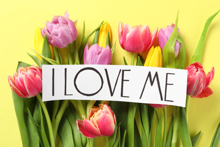 Piece of paper with handwritten phrase I Love Me and tulips on yellow background, flat layの写真素材