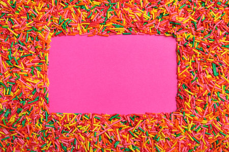 Frame of bright colorful sprinkles on pink background, flat lay with space for text. Confectionery...