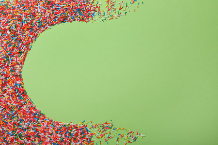 Colorful sprinkles on green background, flat lay with space for text. Confectionery decorの写真素材